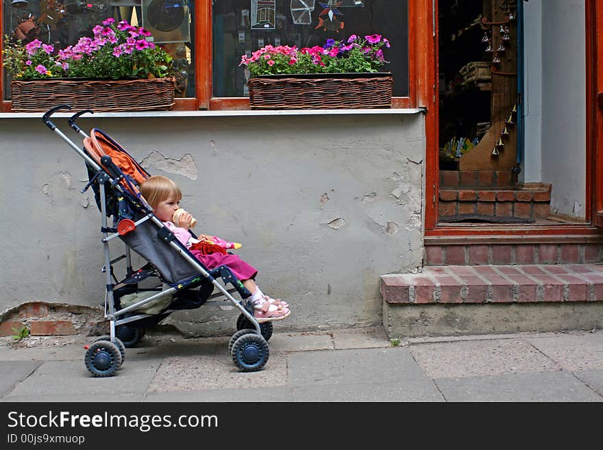 2-3 years old child sitting in the pram in front of the shop doors, eating ice cream and waiting for parent. 2-3 years old child sitting in the pram in front of the shop doors, eating ice cream and waiting for parent