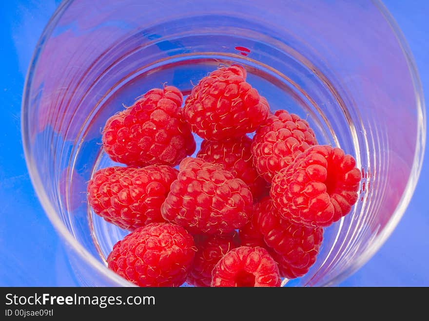 Red raspberry in  glass on  blue background