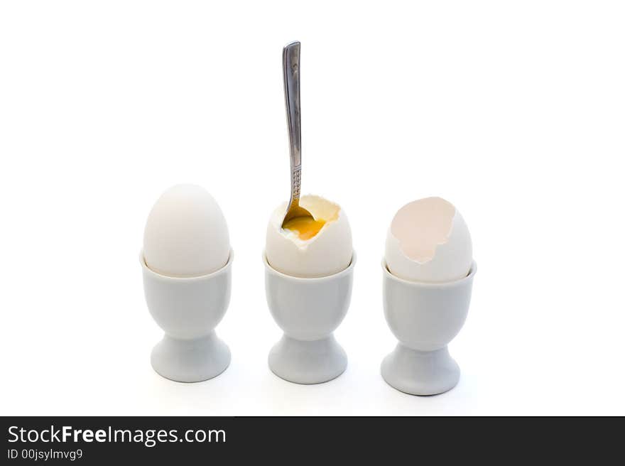 A whole egg, an egg with a spoon and an egg shell in eggcups on white background. A whole egg, an egg with a spoon and an egg shell in eggcups on white background.