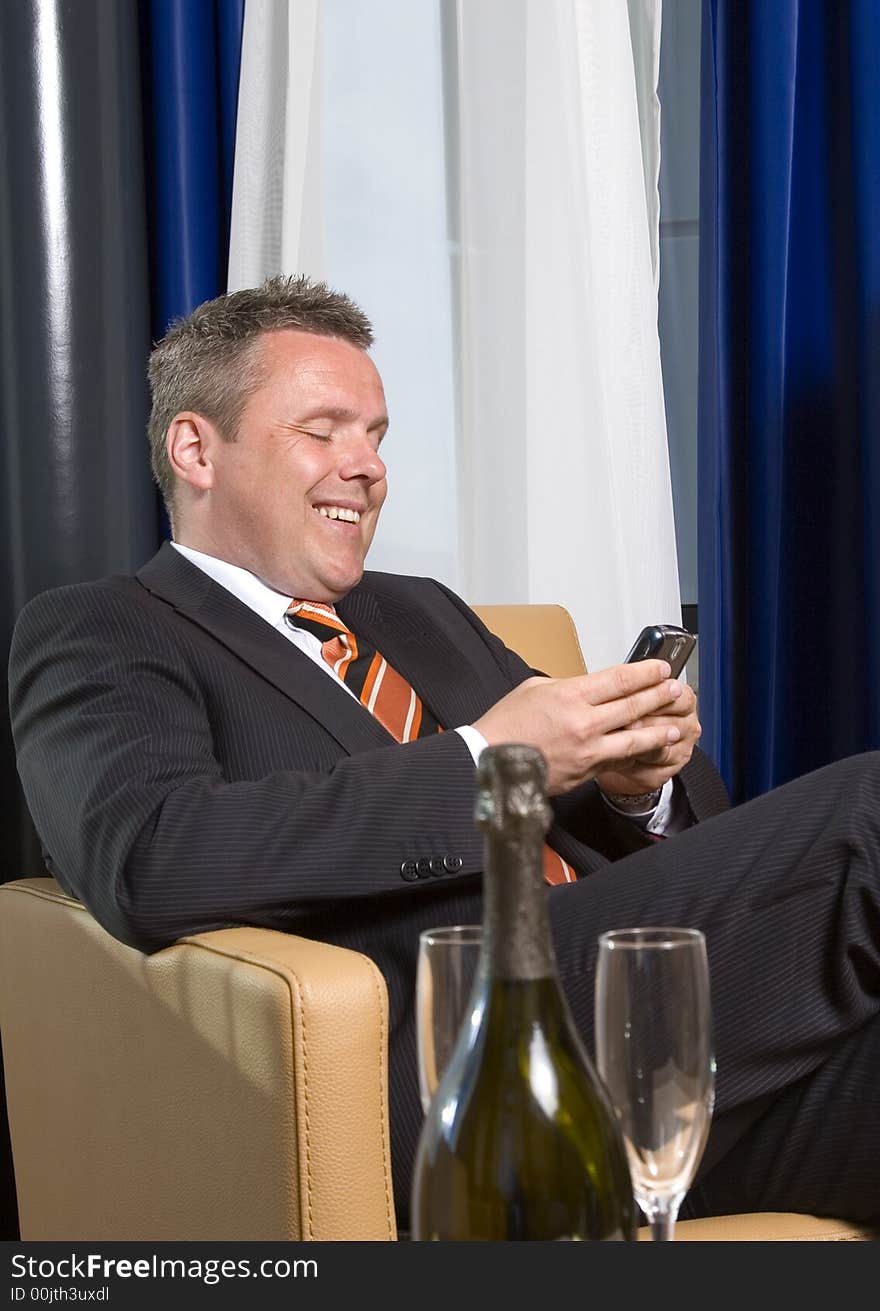 Businessman smiling  texting on his mobile phone, champagne on table. Businessman smiling  texting on his mobile phone, champagne on table