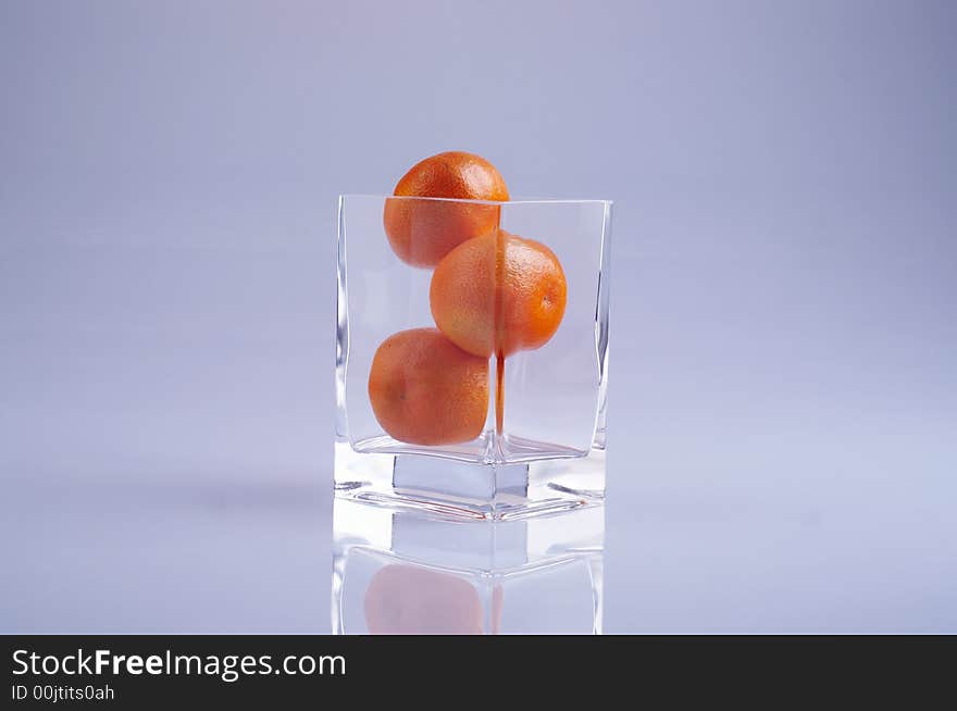 Three tangerines in a glass mirroring on the surface.