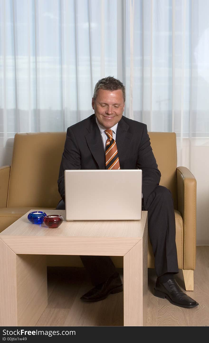 Businessman smiling working on his laptop sitting in sofa. Businessman smiling working on his laptop sitting in sofa