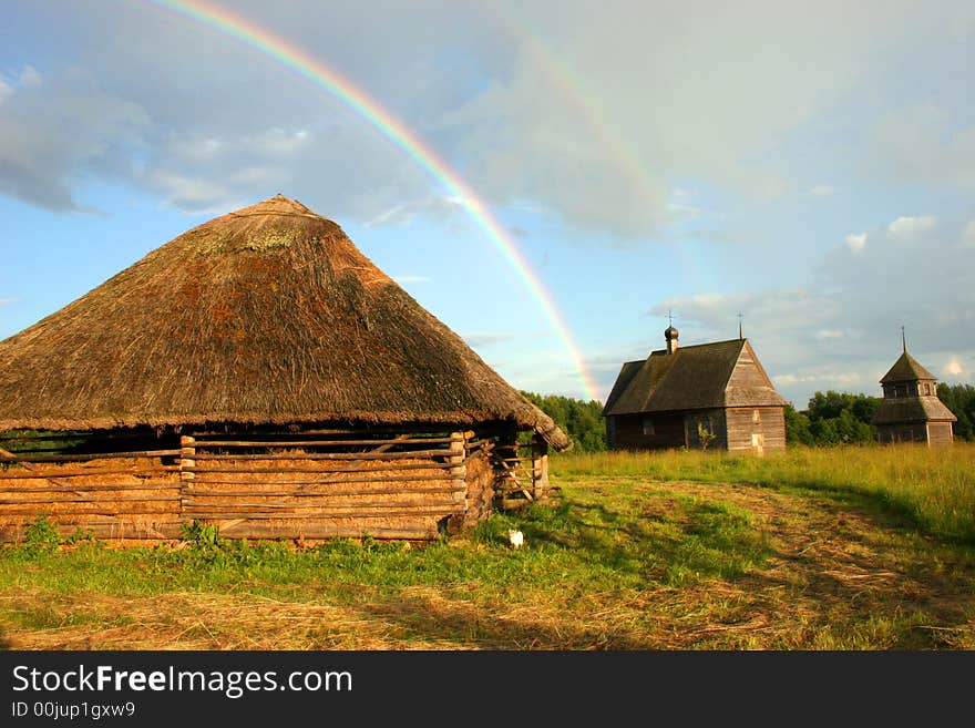 Old wooden small buildings on a background of a rainbow and the dark blue sky. Old wooden small buildings on a background of a rainbow and the dark blue sky