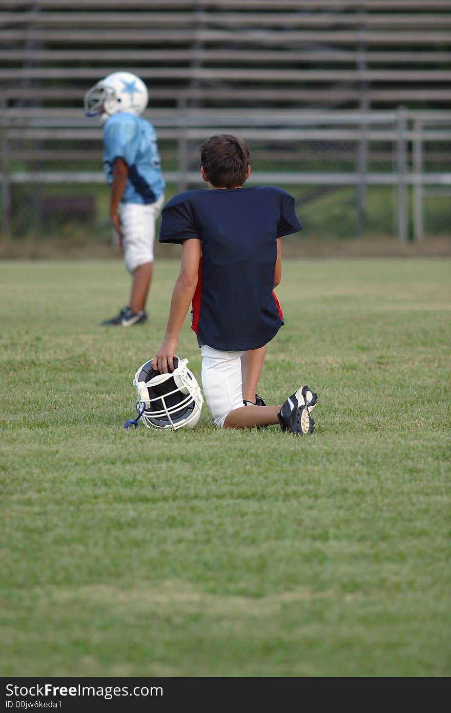 A young boy playing football watches from the sidelines at a game. All logo's and trade names removed from image. A young boy playing football watches from the sidelines at a game. All logo's and trade names removed from image.