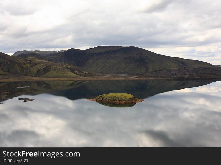 Cloudy sky reflected in the lake inside the  Iceland high hills. Cloudy sky reflected in the lake inside the  Iceland high hills