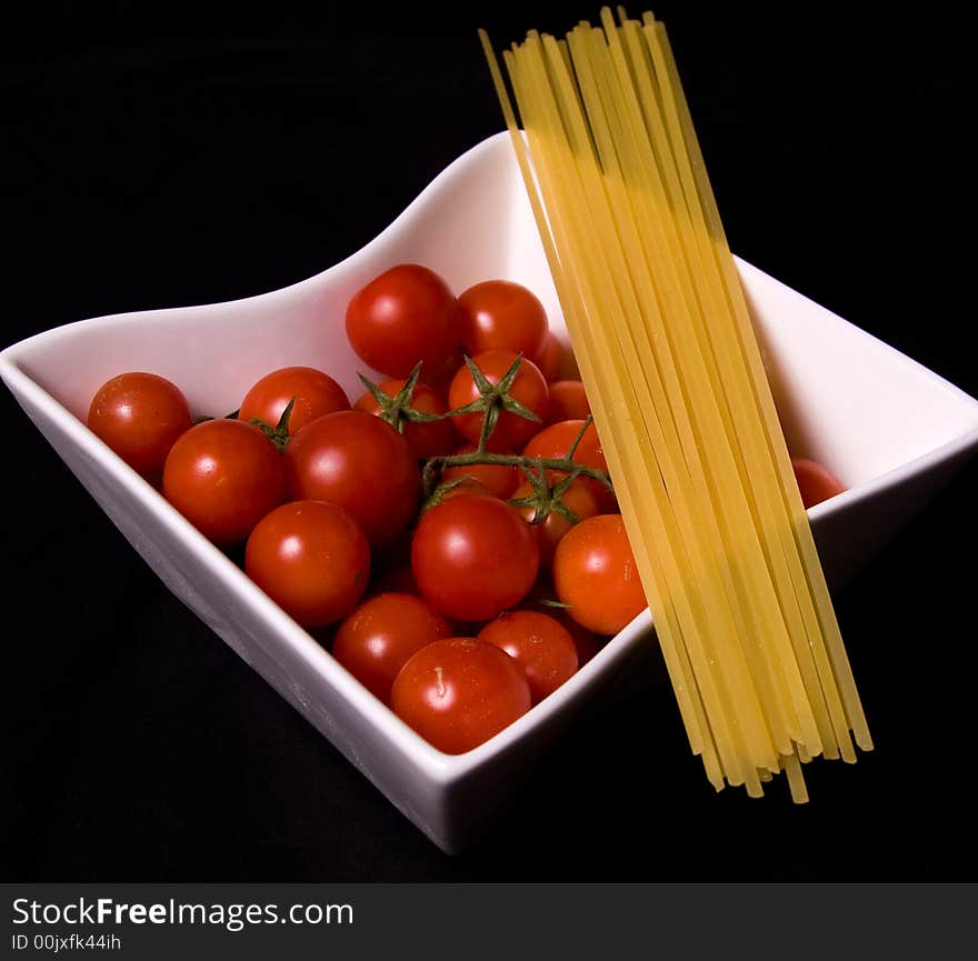 Bowl of ripe red tomatoes with dry pasta noodles against black background. Bowl of ripe red tomatoes with dry pasta noodles against black background.