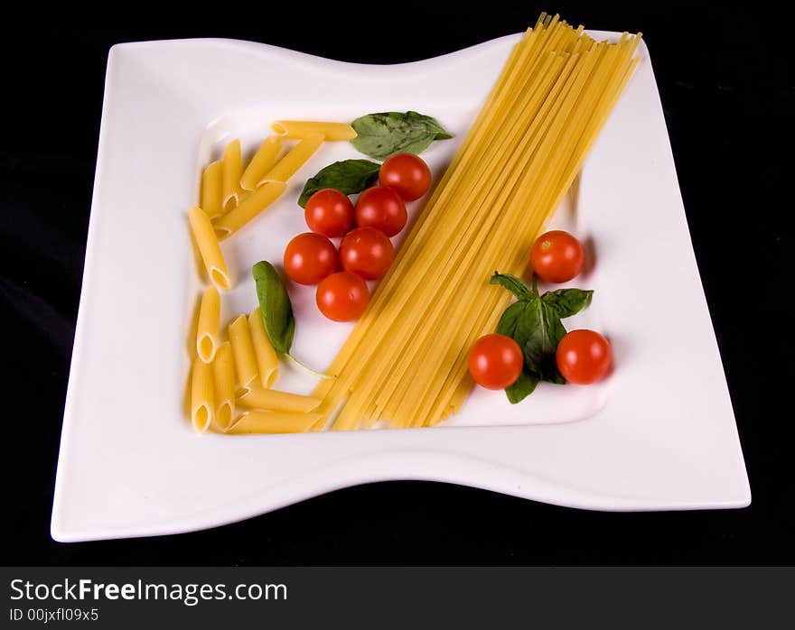 Bowl of uncooked pasta, tomatoes, and basil on black background. Bowl of uncooked pasta, tomatoes, and basil on black background.