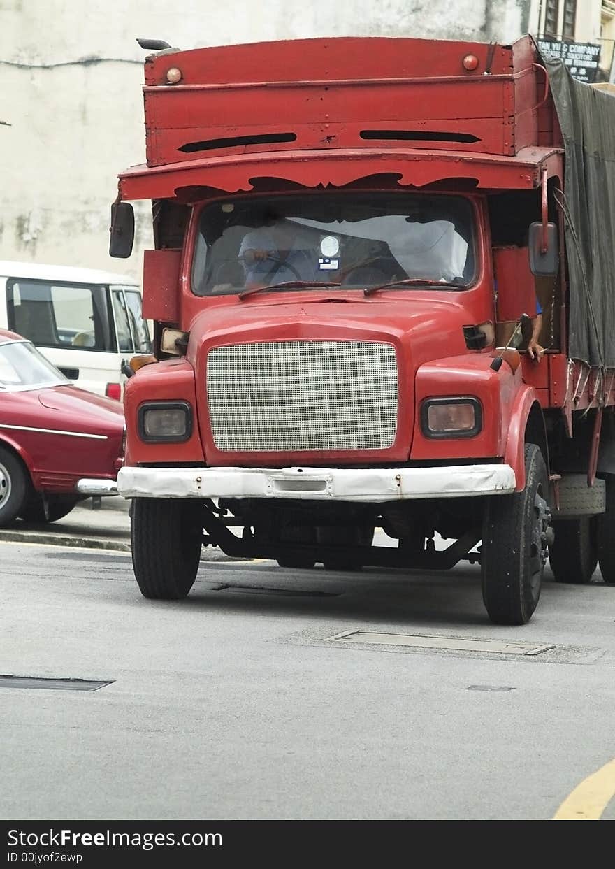 Old red truck driving through a narrow city street.