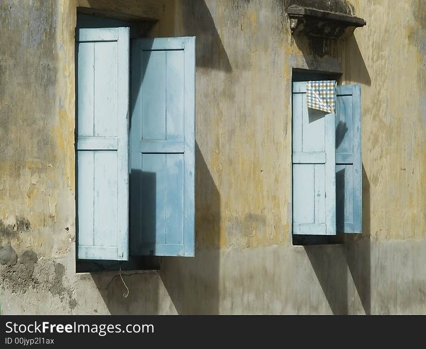 Two windows with open, blue wooden blinds on an old concrete wall. Two windows with open, blue wooden blinds on an old concrete wall