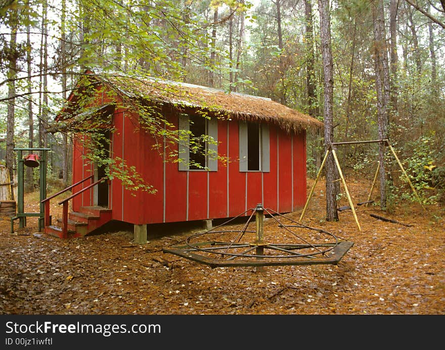 Little Red School House nestled among the trees showing playground equipment in the foreground and a old time school bell in the background