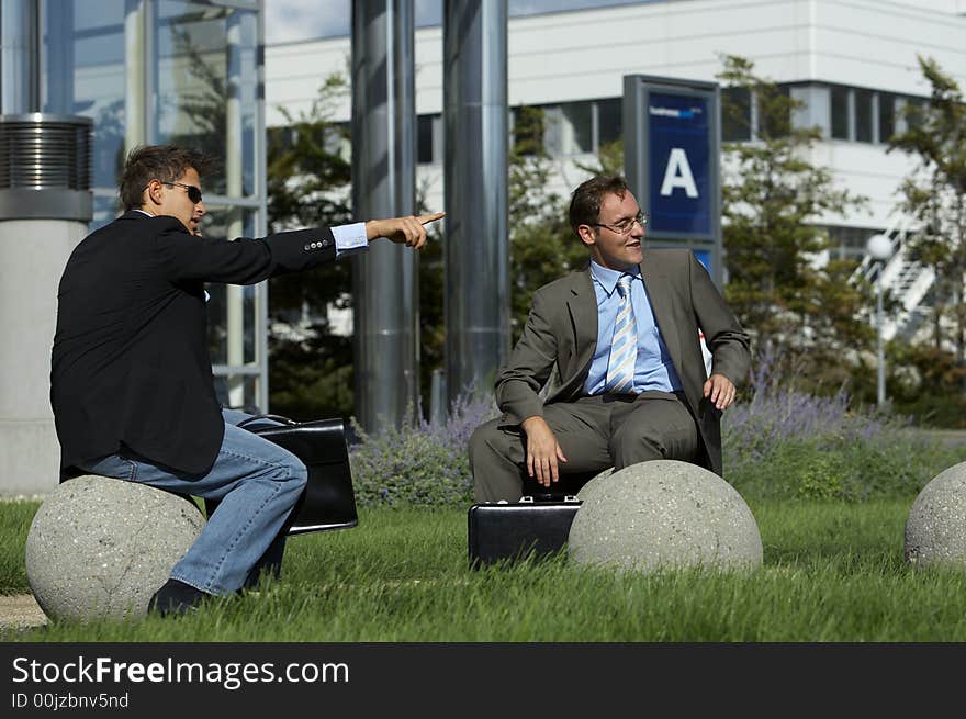 Two young business men sitting outside and pointing on something. Two young business men sitting outside and pointing on something