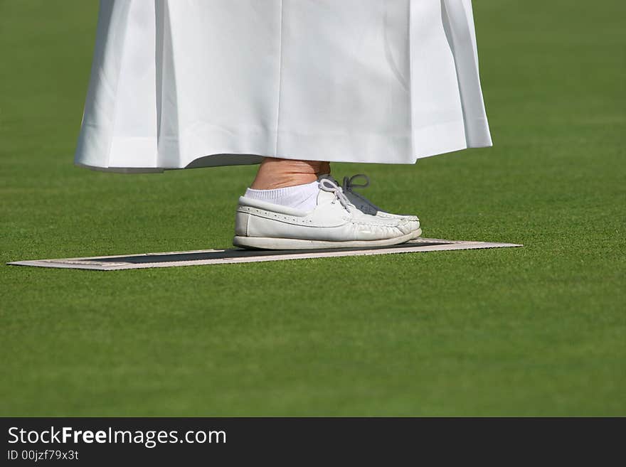 Ankles and feet of an elderly female wearing a long white skirt and white lawn bowling shoes, standing on a mat on a lawned area. Ankles and feet of an elderly female wearing a long white skirt and white lawn bowling shoes, standing on a mat on a lawned area.