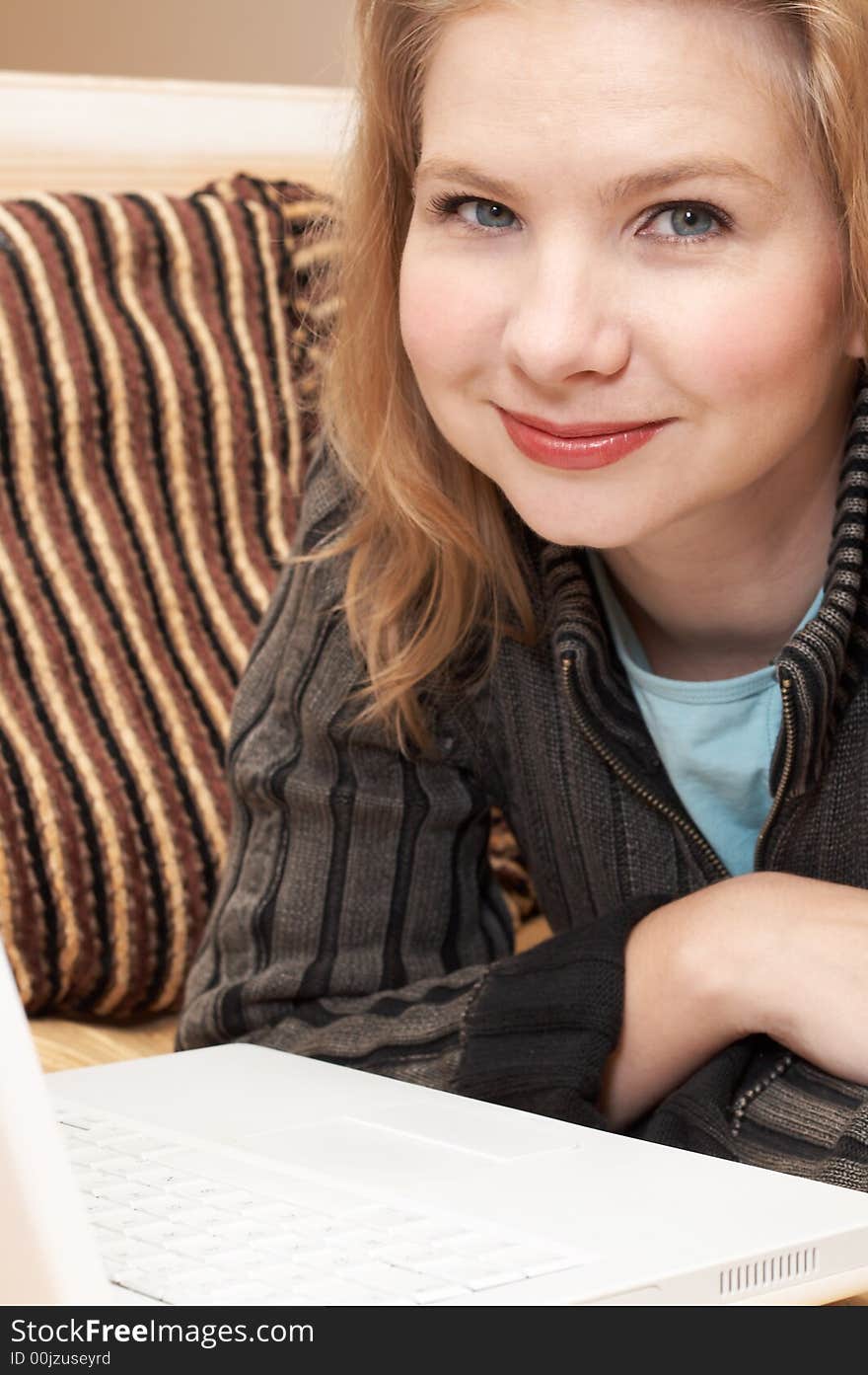 Blonde woman in casual clothes lying on the couch and working on her laptop. Blonde woman in casual clothes lying on the couch and working on her laptop