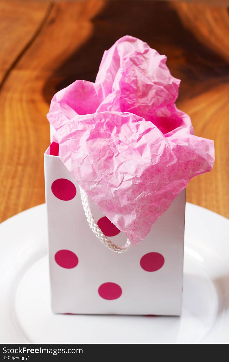 Pink polka-dot colored gift bag on white plate. Pink polka-dot colored gift bag on white plate