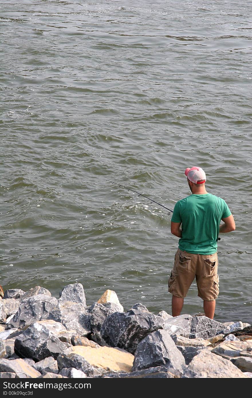 A man on the rocky bank of a river fishing. A man on the rocky bank of a river fishing