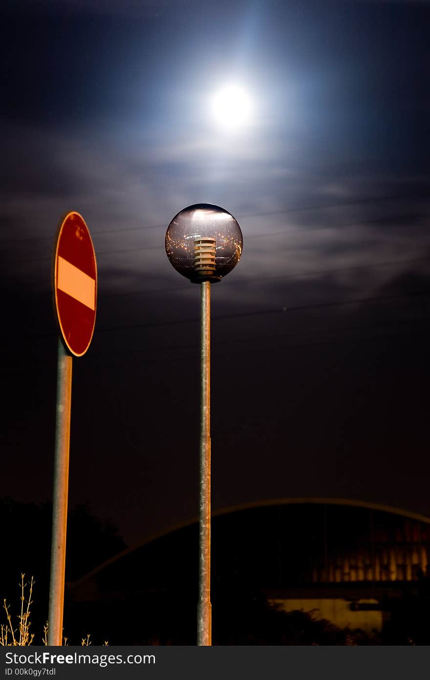 A street light off with a roadsign in the night closer to a factory. A street light off with a roadsign in the night closer to a factory