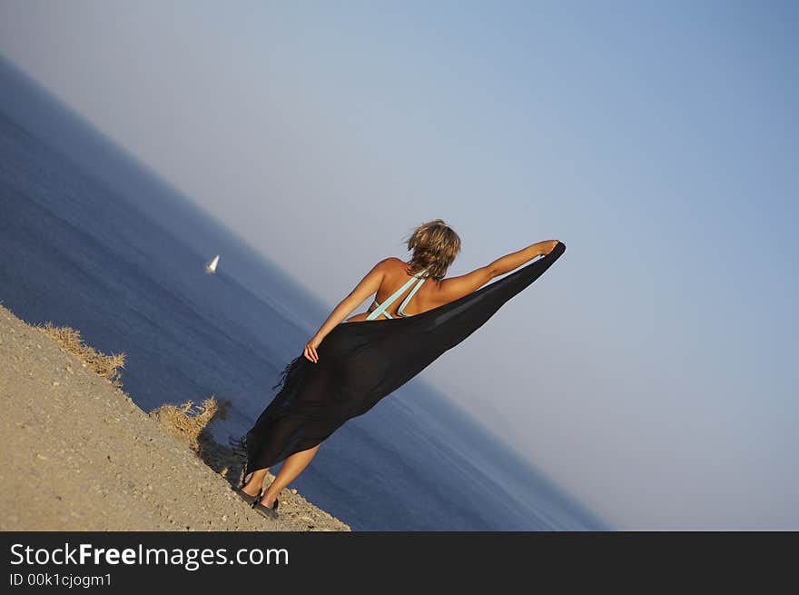 Young woman holding a cloth against the wind on the egde to the sea. Young woman holding a cloth against the wind on the egde to the sea