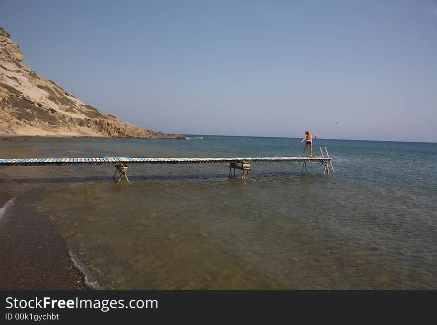 A young boy is standing on a plank and throws rocks into the sea. A young boy is standing on a plank and throws rocks into the sea