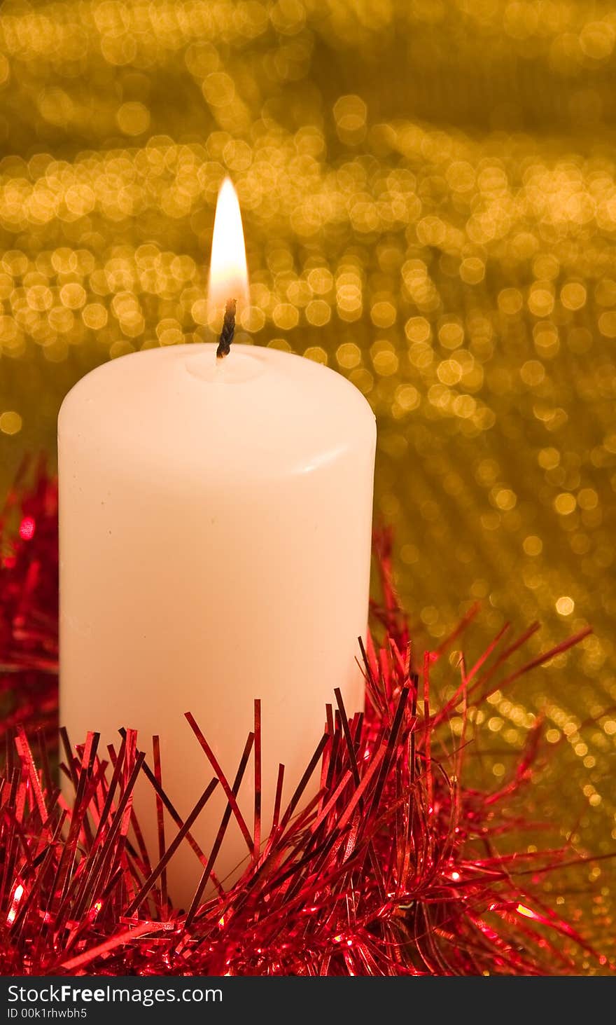 Burning candle with red tinsel in a shimmering golden background. Burning candle with red tinsel in a shimmering golden background