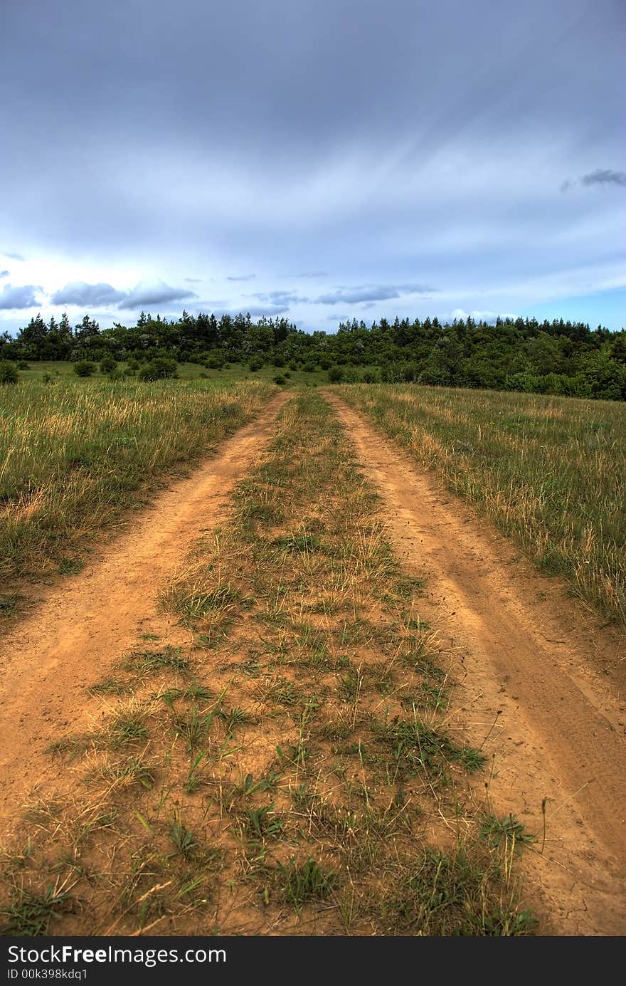 Road to a field. The drama sky above a wood