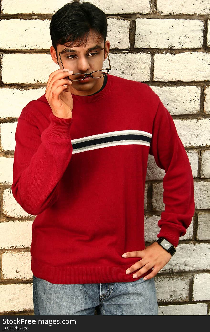 Fashion shoot of young indian man posing with brick background while taking off his glasses. Fashion shoot of young indian man posing with brick background while taking off his glasses