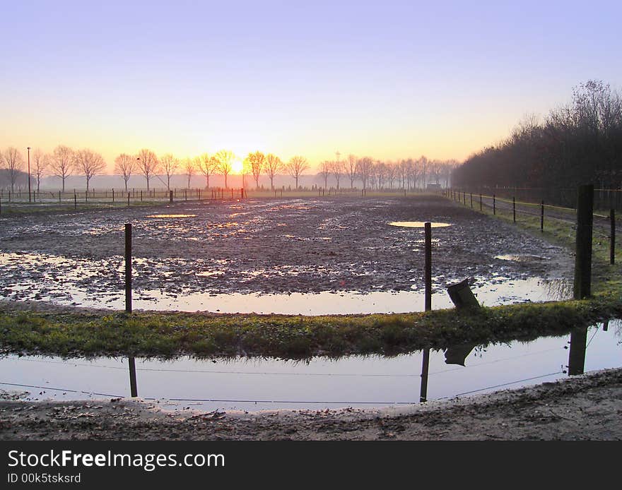 Scenic view of sunset over flooded or waterlogged field in countryside with trees in background. Scenic view of sunset over flooded or waterlogged field in countryside with trees in background.