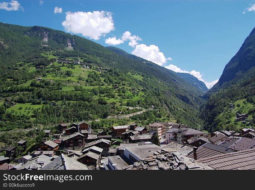 Countryside authentic alpine mountain landscape with green slopes, pastures and village roofs in front. alpes, switzerland; europe. Countryside authentic alpine mountain landscape with green slopes, pastures and village roofs in front. alpes, switzerland; europe