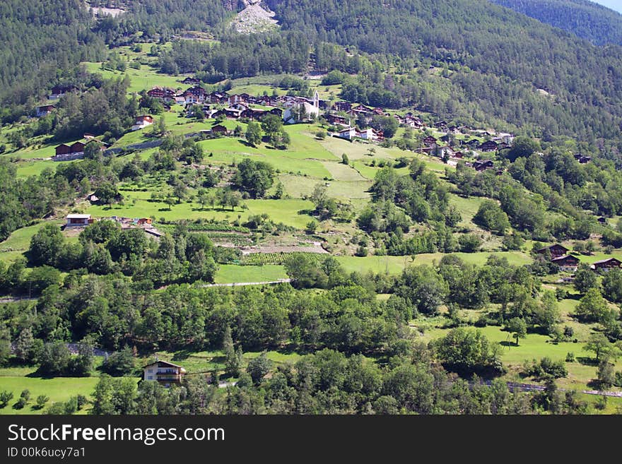 Countryside authentic alpine mountain landscape with green slopes, pastures, trees and village roofs in front. alps, Switzerland; Europe. Countryside authentic alpine mountain landscape with green slopes, pastures, trees and village roofs in front. alps, Switzerland; Europe