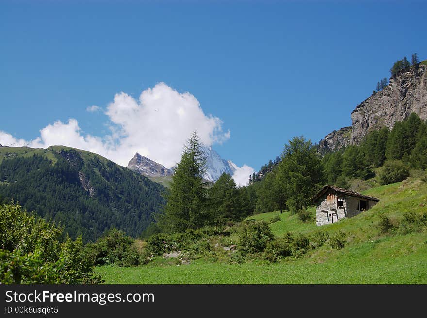 Landscape view on rocky high mountains, green trees, slopes, clouds and obsolete wooden house in summer. Zermat, Switzerland, europe. Landscape view on rocky high mountains, green trees, slopes, clouds and obsolete wooden house in summer. Zermat, Switzerland, europe.