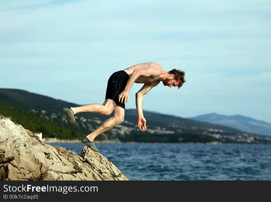 A young man summersaults from a cliff into the sea!. A young man summersaults from a cliff into the sea!