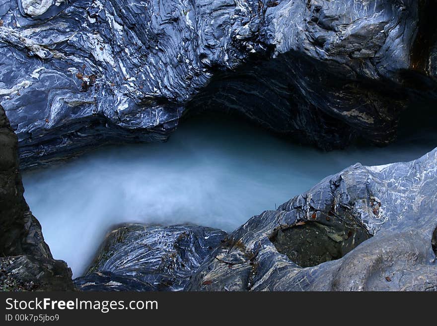 Motion-blurred water stream between massive rocks with interesting structure.