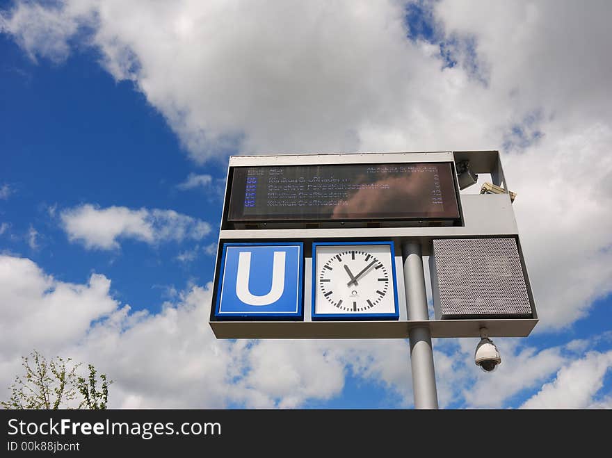 Subway sign with clock against sky