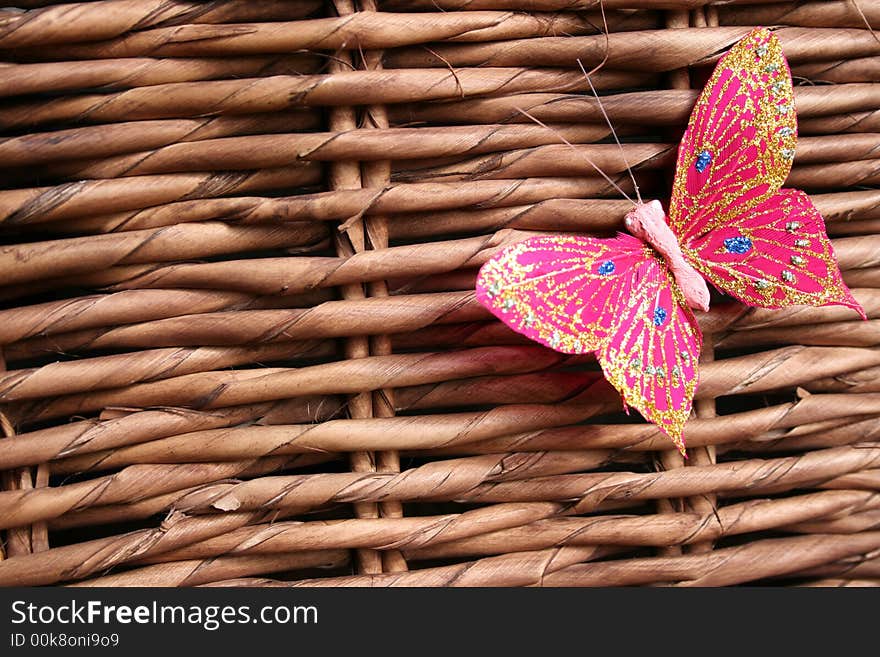 Pink butterfly decorated with glitter on a woven wood background. Pink butterfly decorated with glitter on a woven wood background