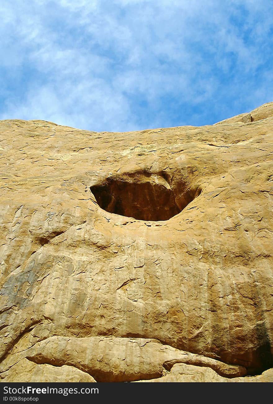 Blue sky and fluffy clouds above beautiful sandstone cliff with enticing round cave. Blue sky and fluffy clouds above beautiful sandstone cliff with enticing round cave