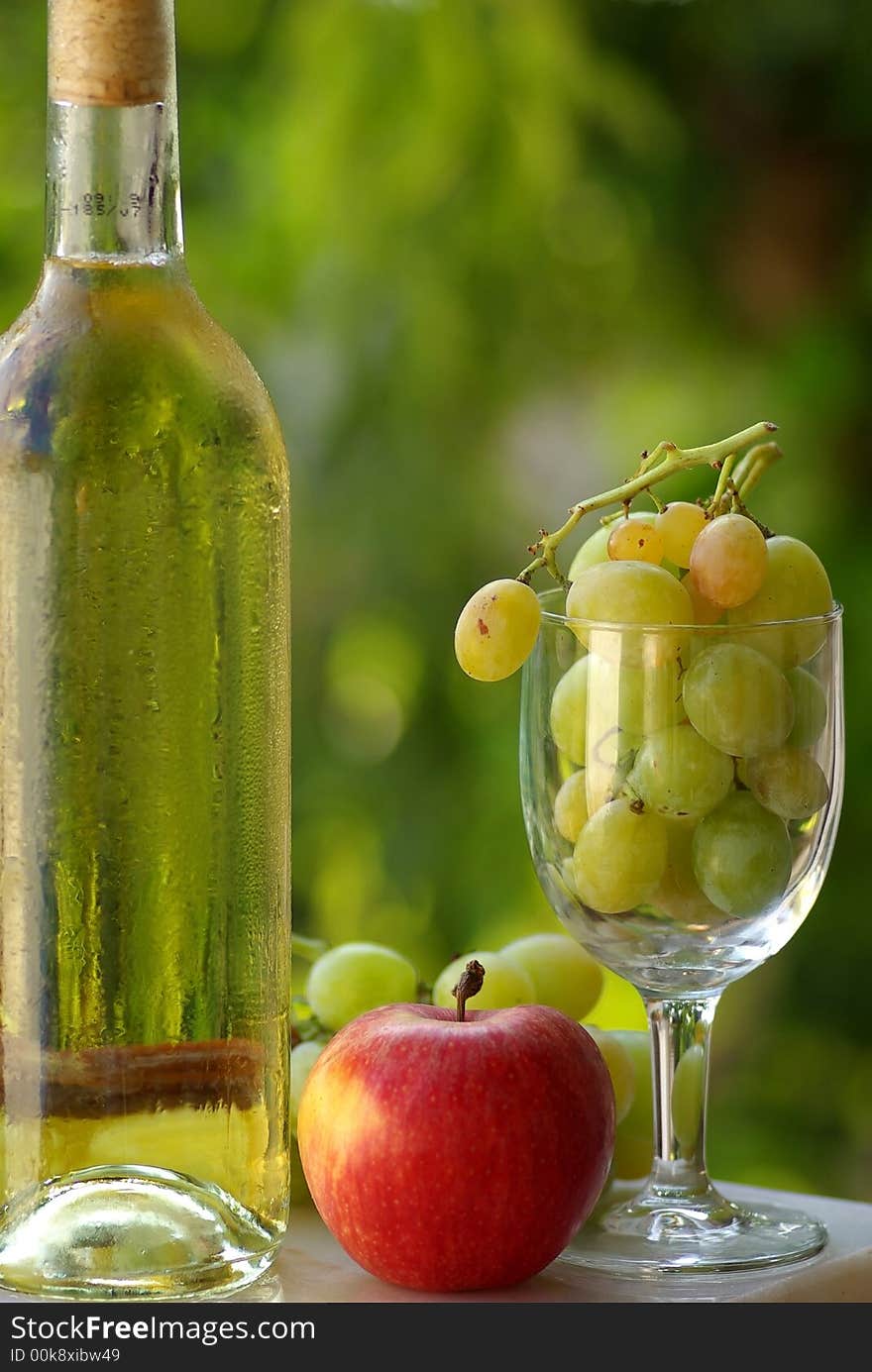 Bottle of white wine and fruit with full glass of grapes.