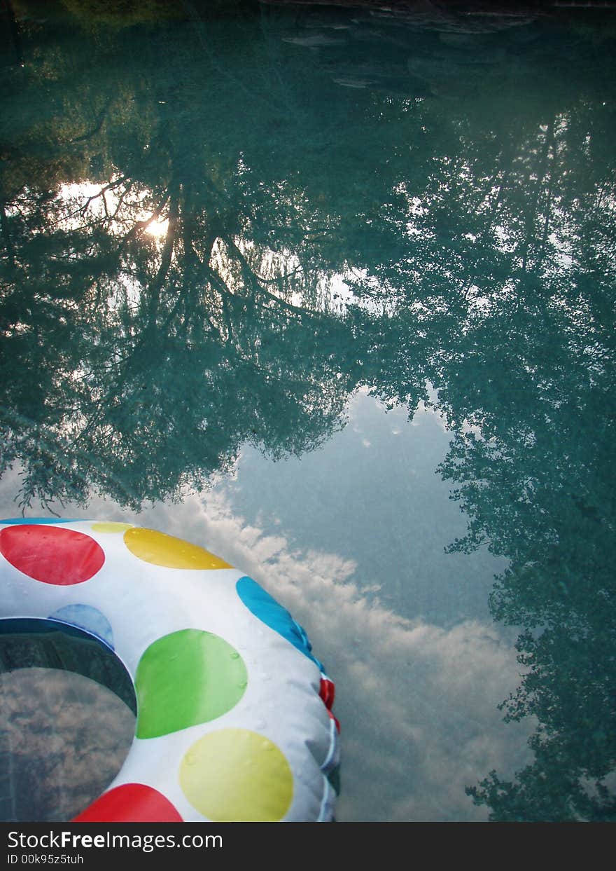 Child's innertube floating in a pool, reflecting an evening sun and trees. Child's innertube floating in a pool, reflecting an evening sun and trees.