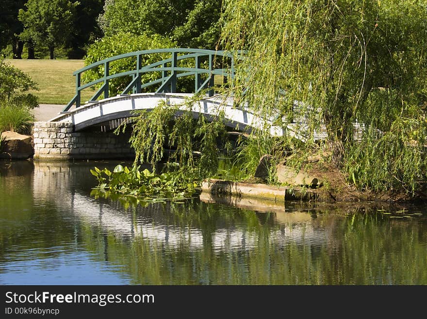 Footbridge crossing over a pond on a calm day projects a reflection of the bridge on the water