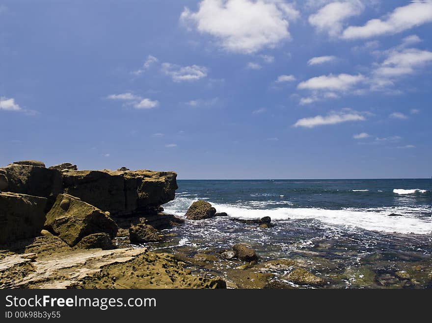 Ocean surf at low tide against a rock shoreline with deep blue sky