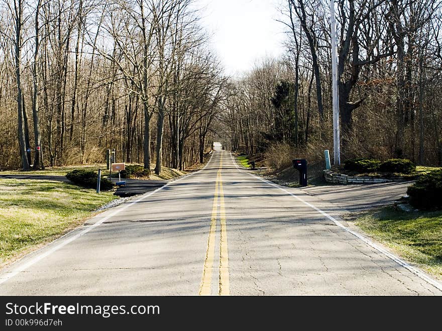 Double yellow line divides lanes on a country road in winter with barren trees