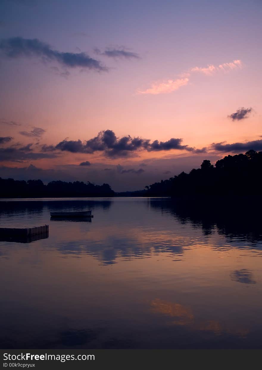 Boat moored off a pier in a reservoir used for kayak and canoe competition and training as seen just after the sun have descended below the horizon. Boat moored off a pier in a reservoir used for kayak and canoe competition and training as seen just after the sun have descended below the horizon.