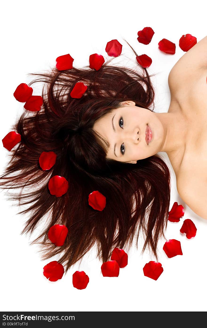 A young Asian woman lying on the studio floor with red rose petals. A young Asian woman lying on the studio floor with red rose petals