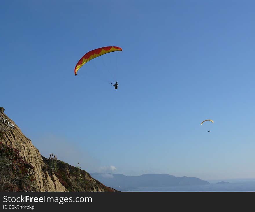 Two daring gliders having a great time catching thermals. At a cliff south of San Francisco on nice summer afternoon. Blue ocean and mountains in the background.