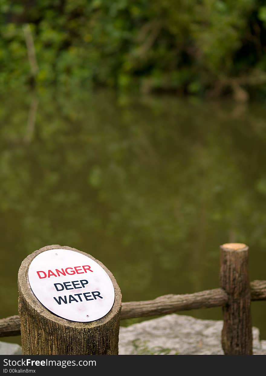 Elliptical aluminum plate etched with the words Danger, in red, and Deep Water, in black, besides a disused quarry, that is flooded. Elliptical aluminum plate etched with the words Danger, in red, and Deep Water, in black, besides a disused quarry, that is flooded.