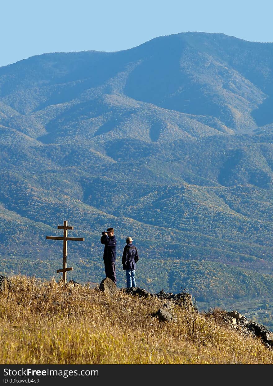 Fall panorama landscape with two hikers standing on the mountain top near the christian rood. Fall panorama landscape with two hikers standing on the mountain top near the christian rood