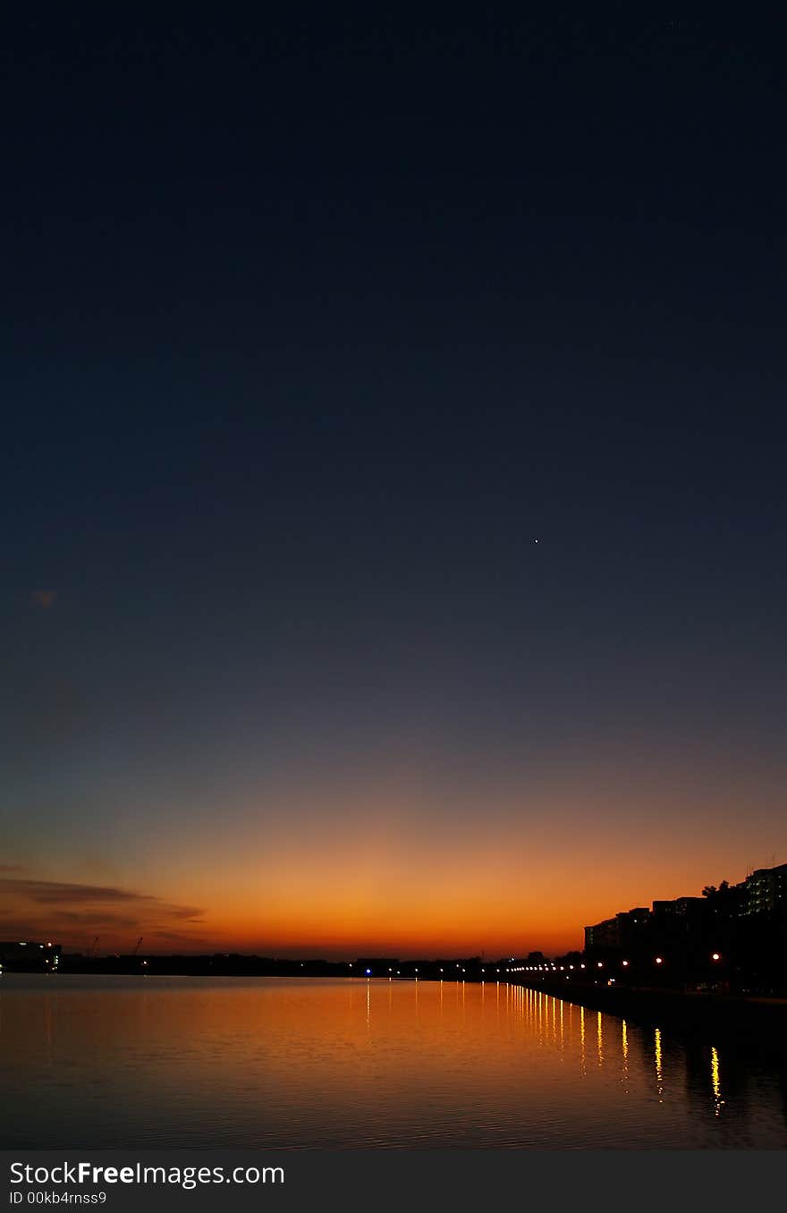 Day glow long after the sun has set in a cloudless sky over a reservoir edged with heavy industry and an apartment complex. The evening star Venus is visible in the sky. Day glow long after the sun has set in a cloudless sky over a reservoir edged with heavy industry and an apartment complex. The evening star Venus is visible in the sky.