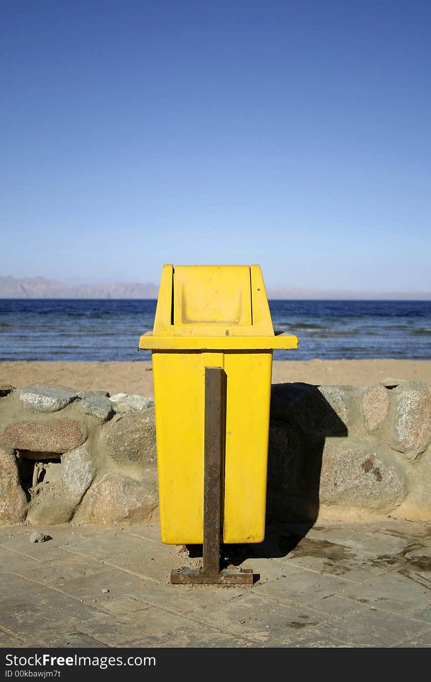 Yellow dustbin on wallway by seaside