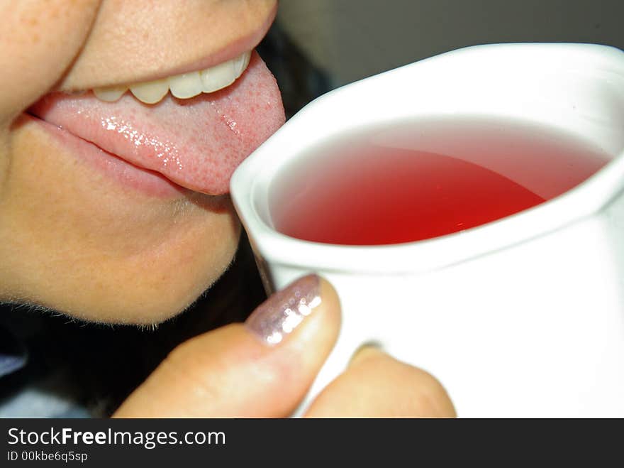 A girl tasting a red fruit tea from a white tea cup. A girl tasting a red fruit tea from a white tea cup