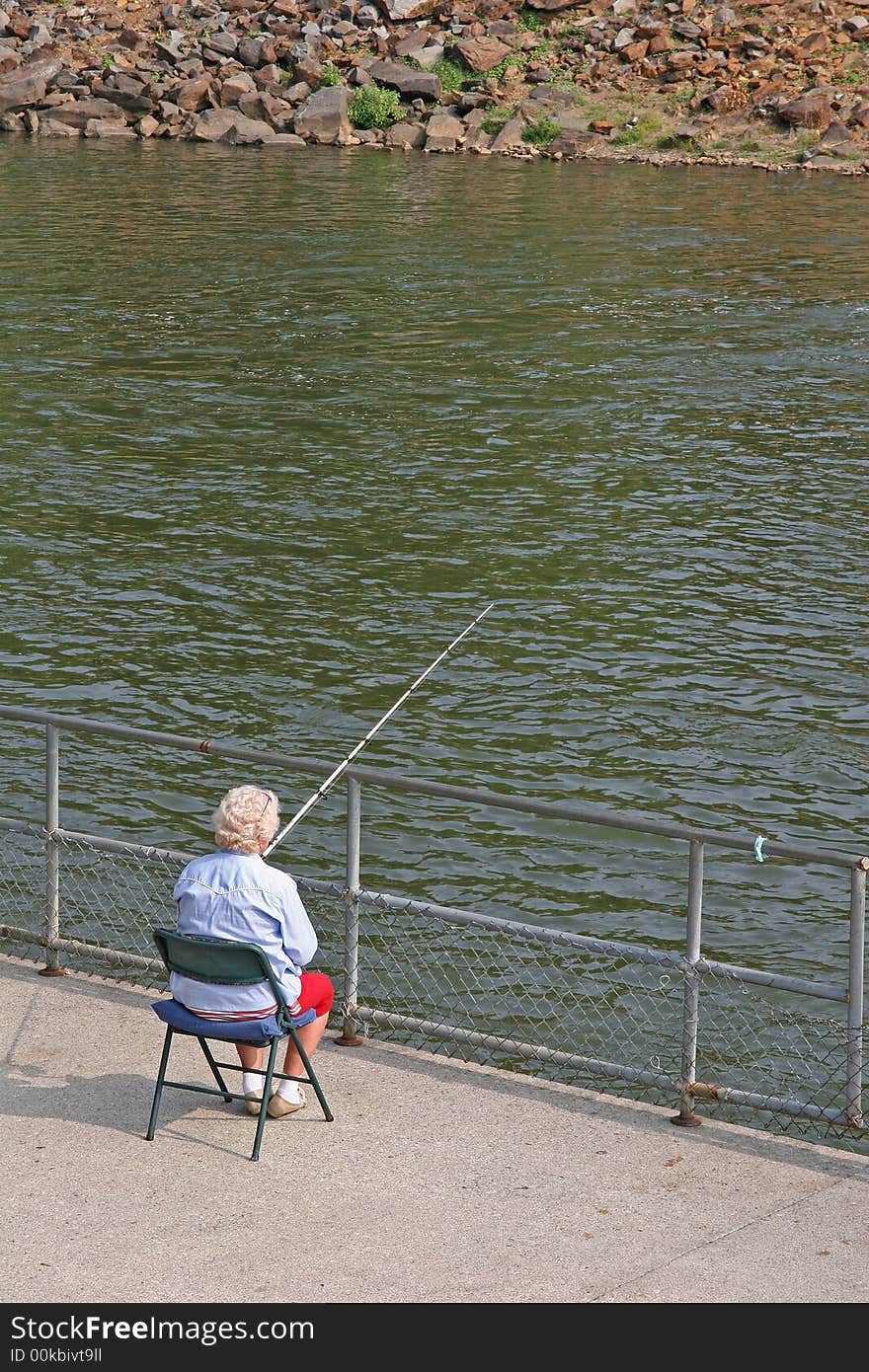 An old women sitting in a chair by the river fishing. An old women sitting in a chair by the river fishing