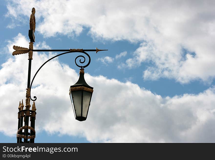 Antique lamp column is photographed against blue sky with white clouds