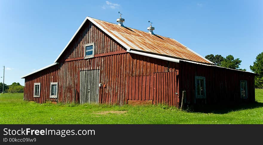 Old red barn against blue sky with green grass in front